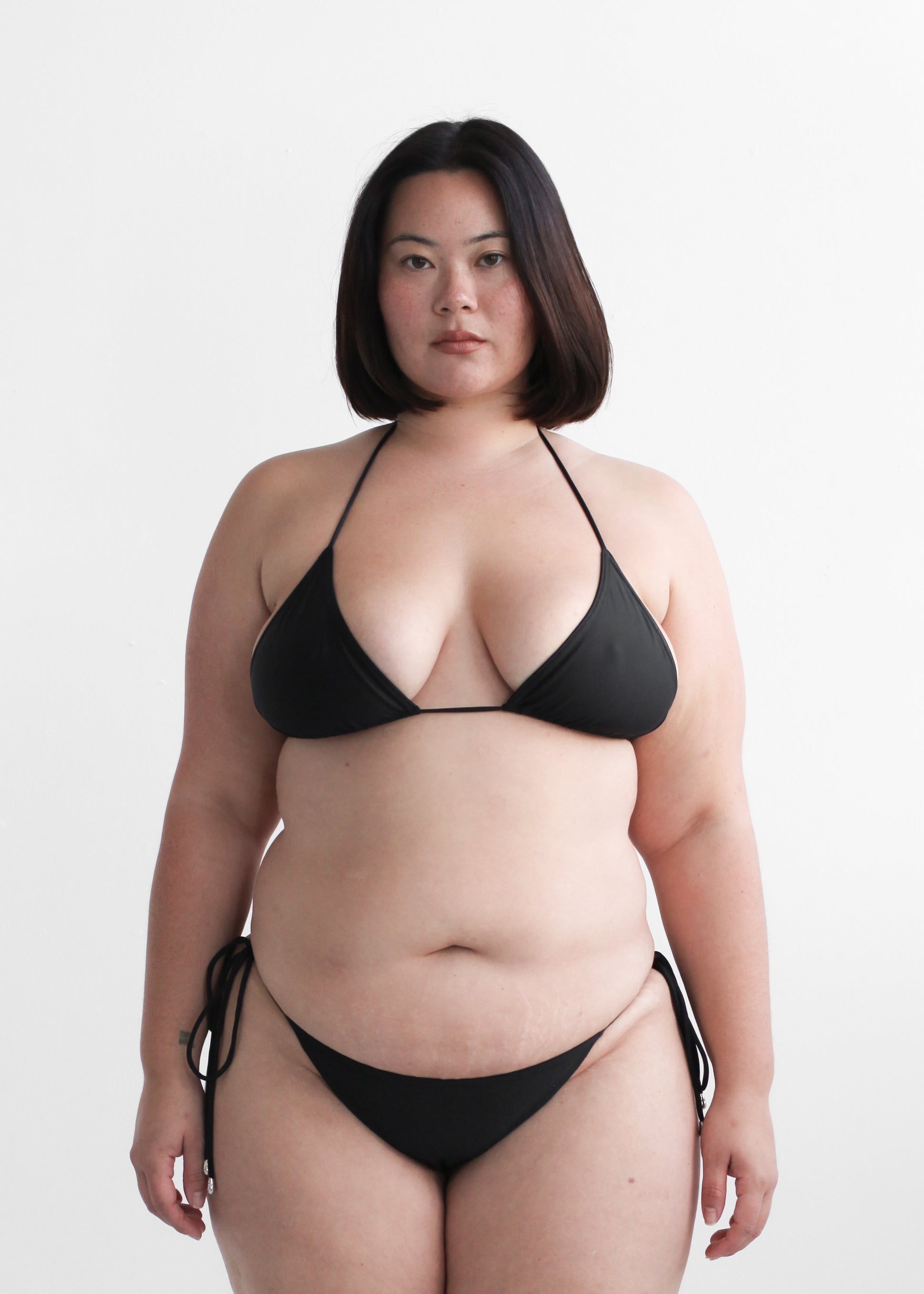 Plus size women's black triangle halter bikini top and tie-side bottoms with silver hardware, front view