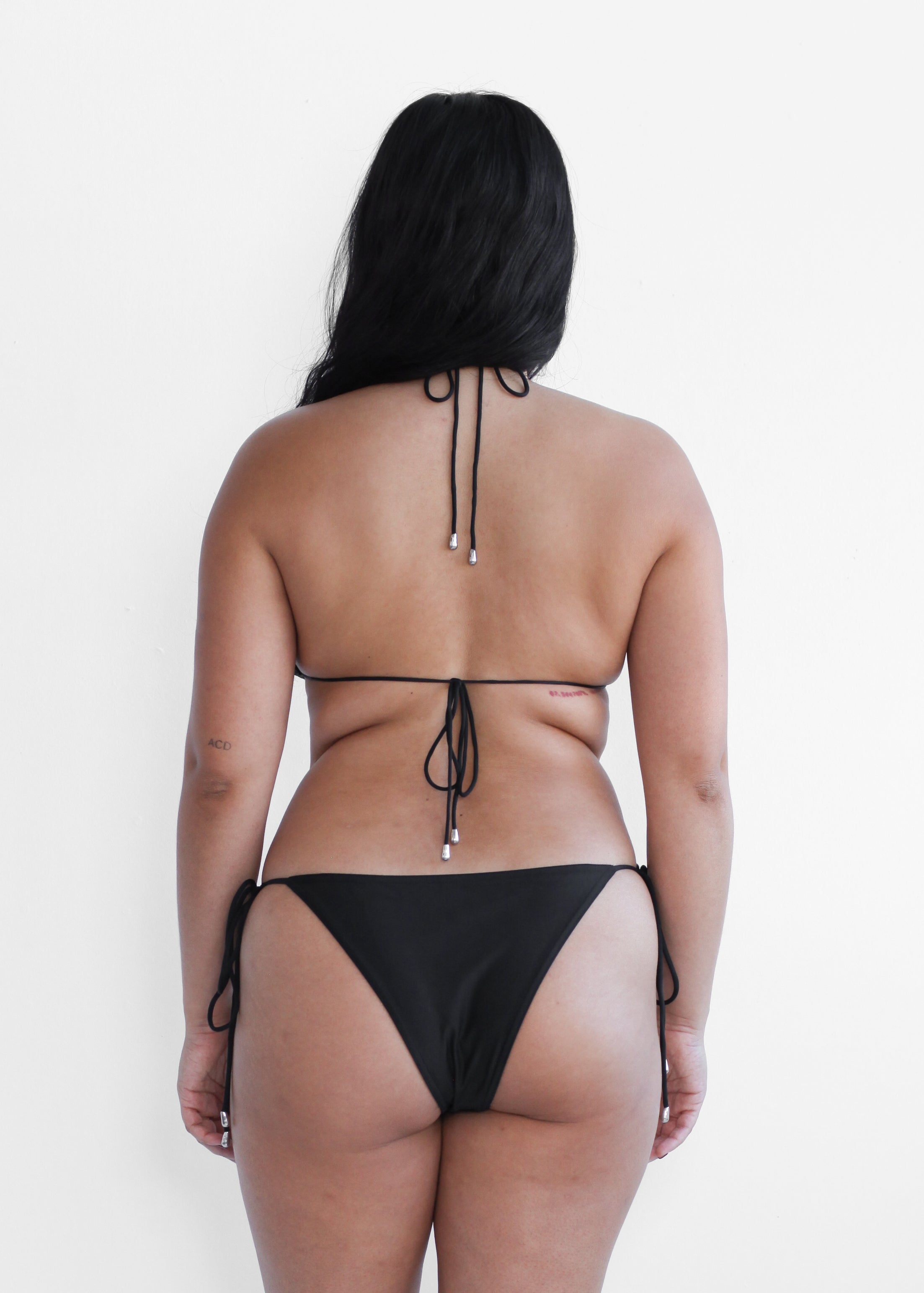 Size inclusive women's black triangle halter bikini top and tie-side bottoms with silver hardware, back view